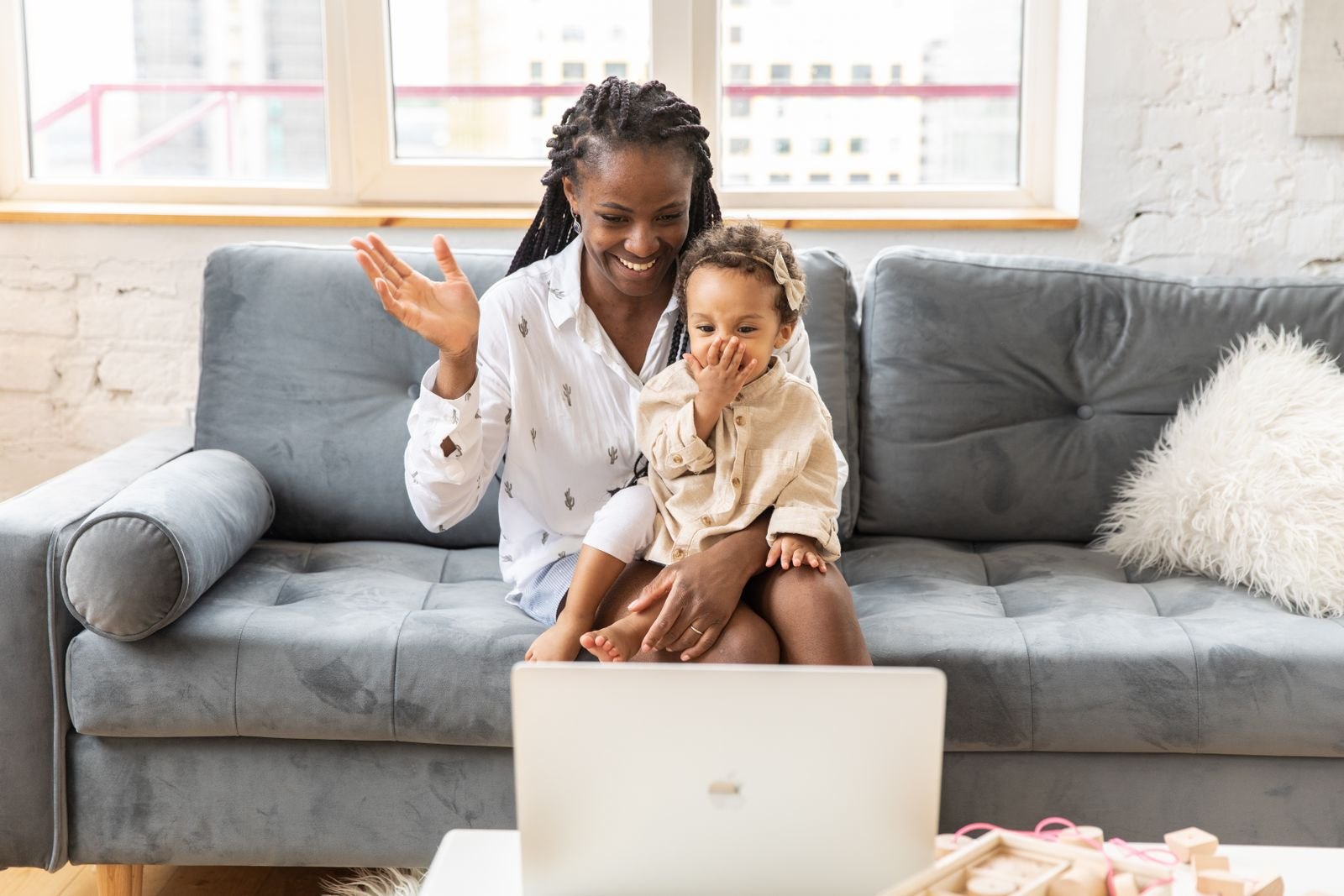 A mother and her young daughter waving to their therapist during an online video session